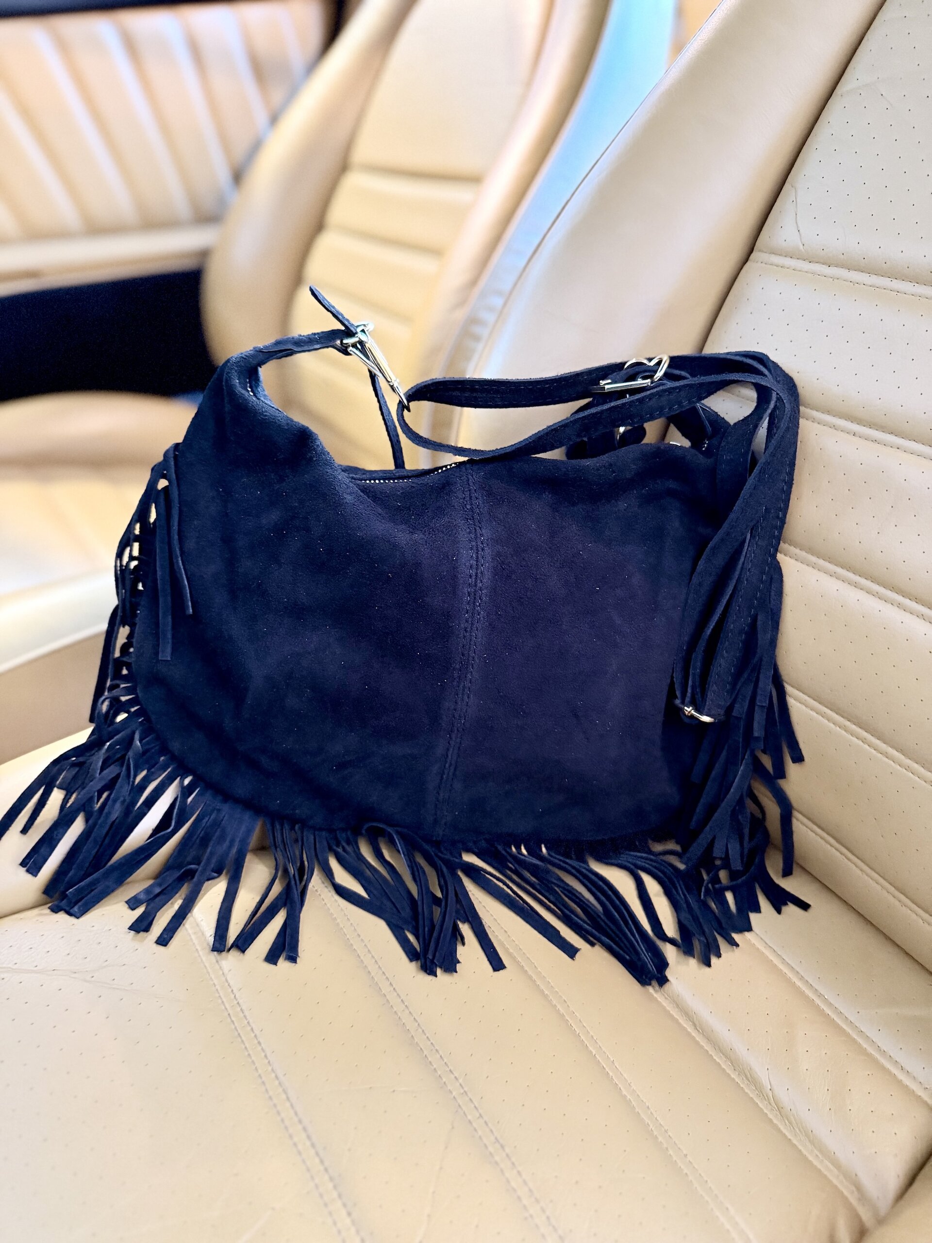 Wildleder Tasche mit Fransen in Schwarz auf einem hellen Ledersitz
