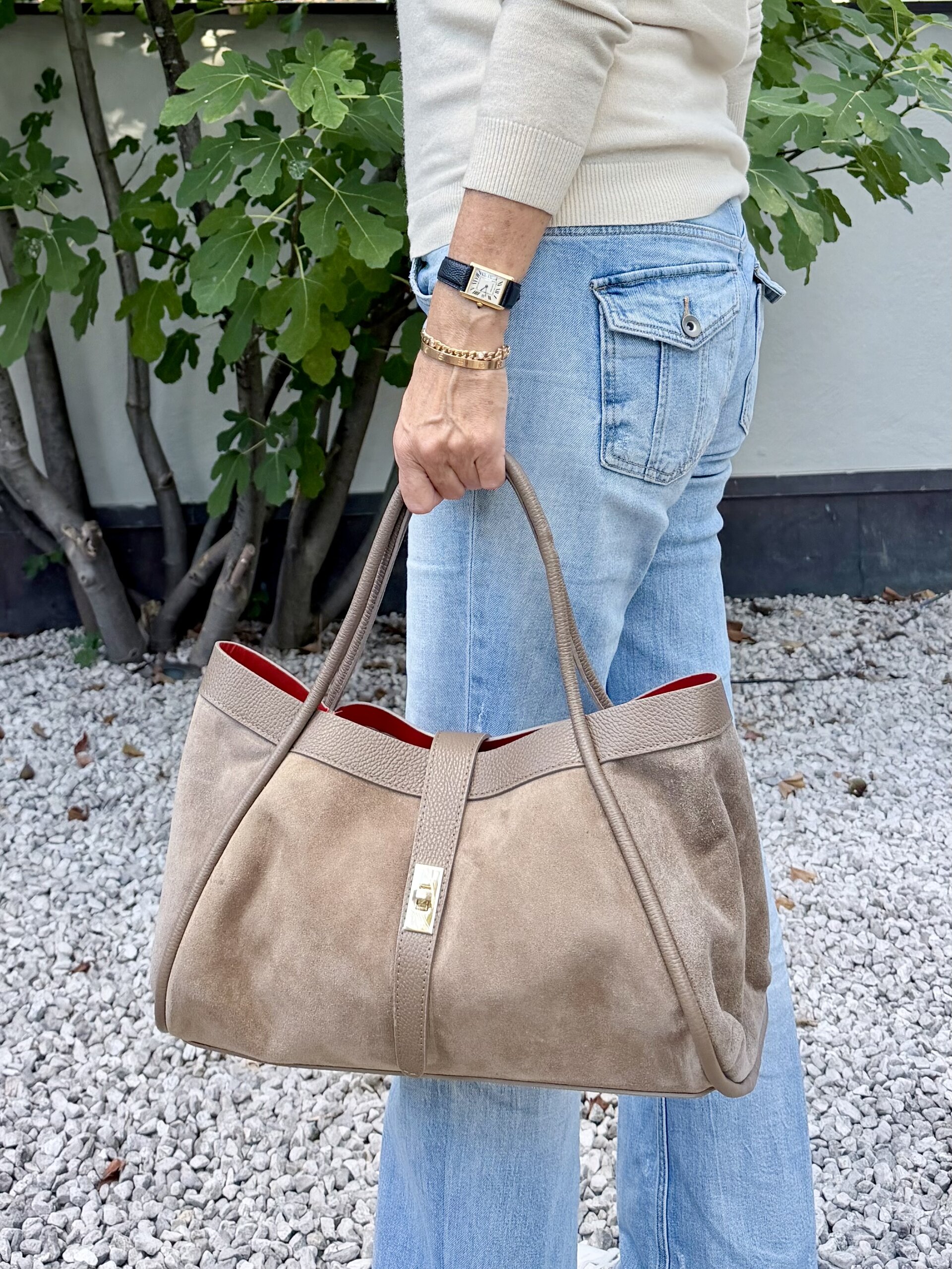 Wildleder Handtasche in Taupe mit rotem Innenfutter, in der Hand getragen zu Jeans