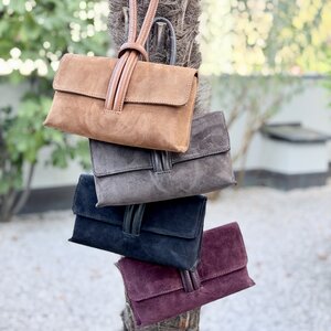 Wildleder Schlaufen Clutch in Cognac, Dunkelbraun, Schwarz und Bordeaux, an einem Palmenstamm hängend